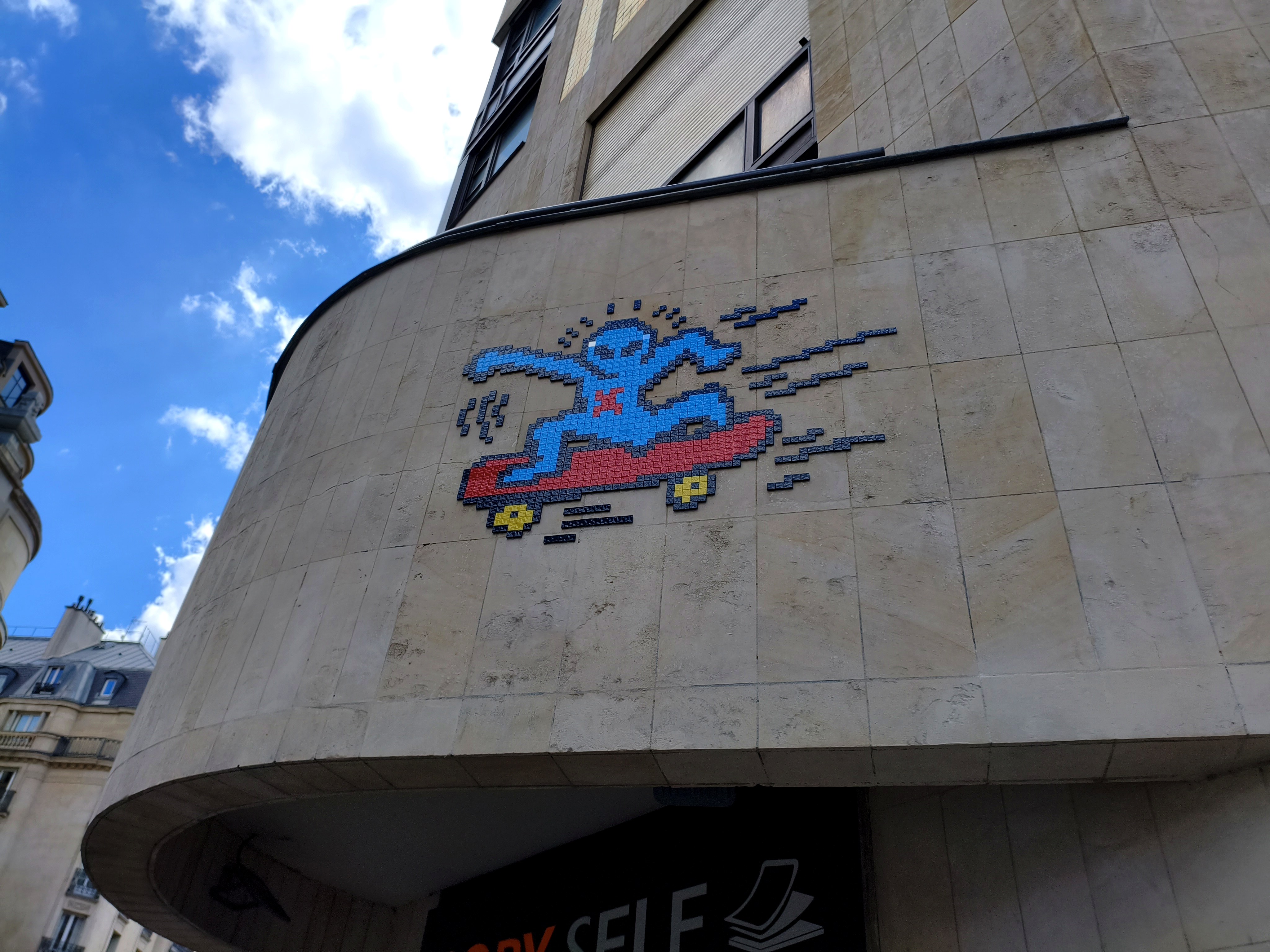 Mosaïque de street art en pixels représentant un personnage bleu sur une planche rouge, sur un immeuble du centre de Paris