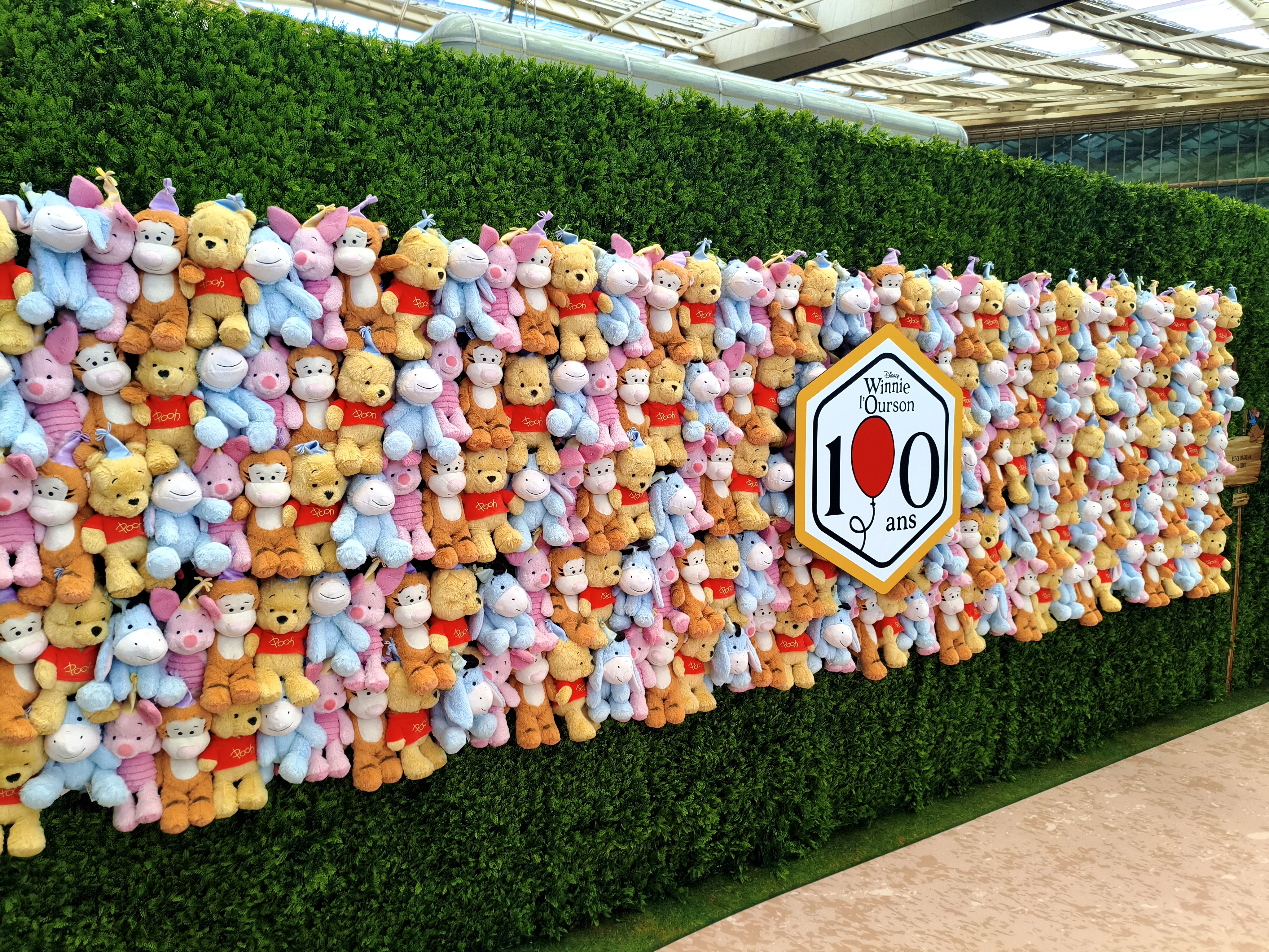 Mur végétal couvert de peluches Winnie l'Ourson, Porcinet, Tigrou et Bourriquet avec le logo des 100 ans