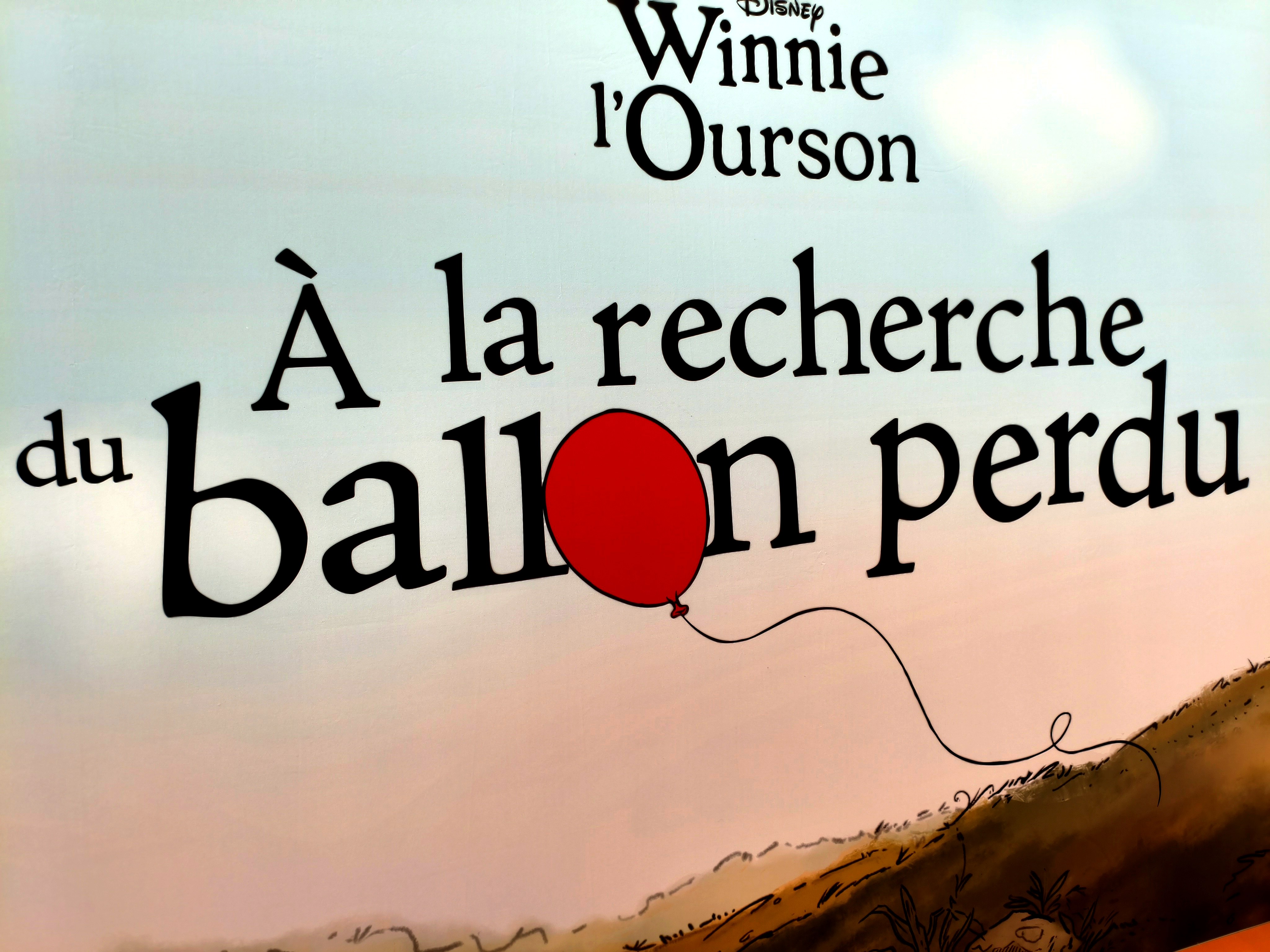 Panneau du titre de l'exposition Winnie l'Ourson À la recherche du ballon perdu avec le ballon rouge